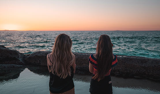 Two girls stand in front of the ocean